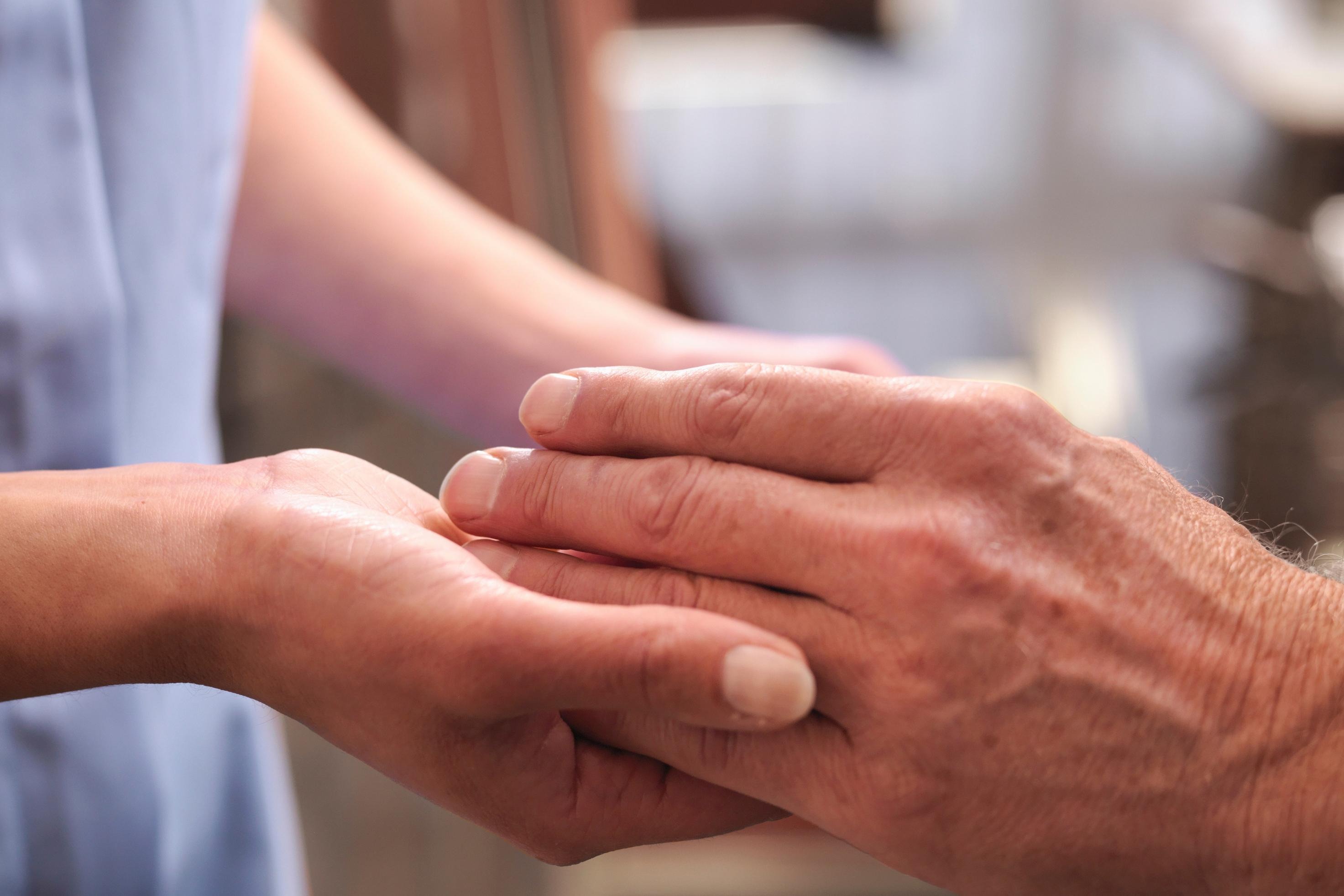 Vårdbiträde som håller äldre person i handen